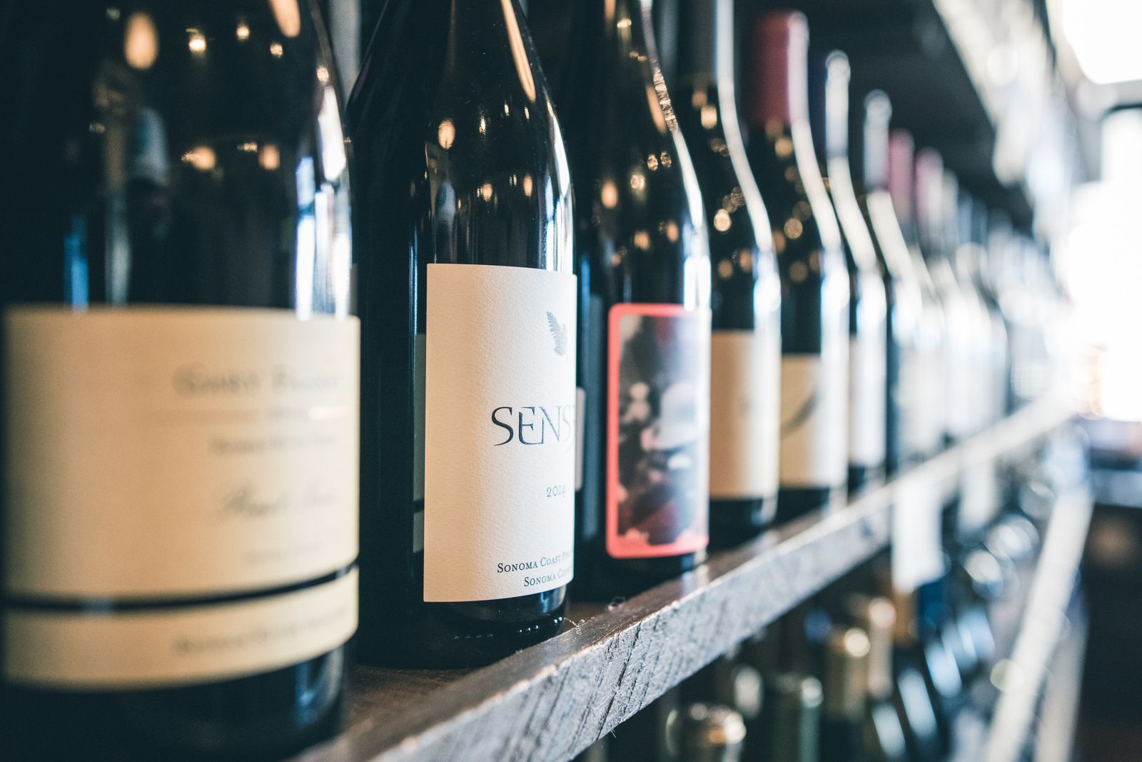 A row of wine bottles on a wooden shelf, seen up close.